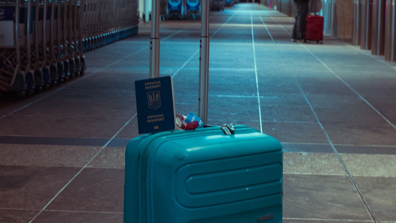 A teal suitcase standing in an empty airport concourse, ready for the next flight